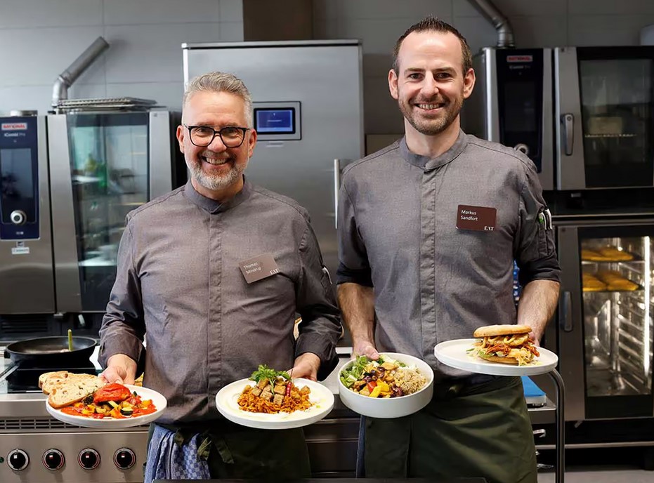 Thomas Mindrup (l. im Bild) und Markus Sandfort (r. im Bild) vom EAT-Team präsentieren die KI-gerierten Gerichte Ägyptischer Koshari, das Piri-Piri Hühnchen, die Quinoa-Bowl und den Hawaii-Burger. Sie stehen im April auf dem Speiseplan im EAT.